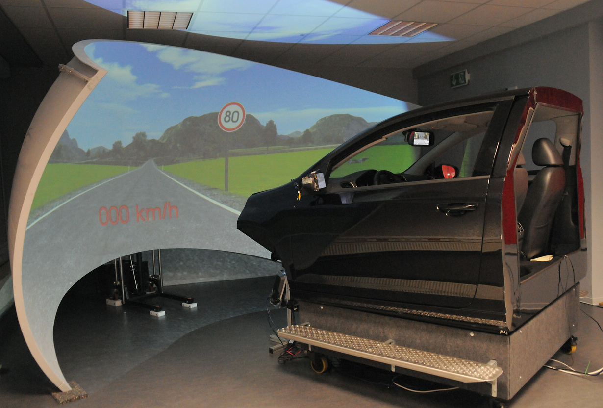 Fahrsimulator mit Autokabine und Bildschirm, der eine Straße mit 80 km/h Schild zeigt.